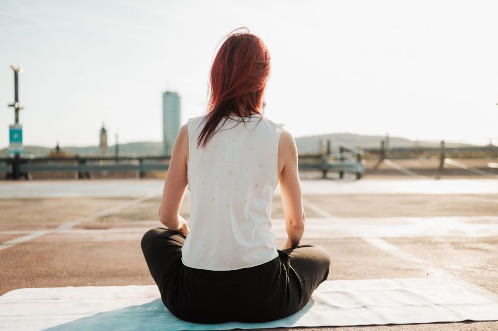 Person in white shirt and black pants sits cross-legged on wooden deck during golden sunset.