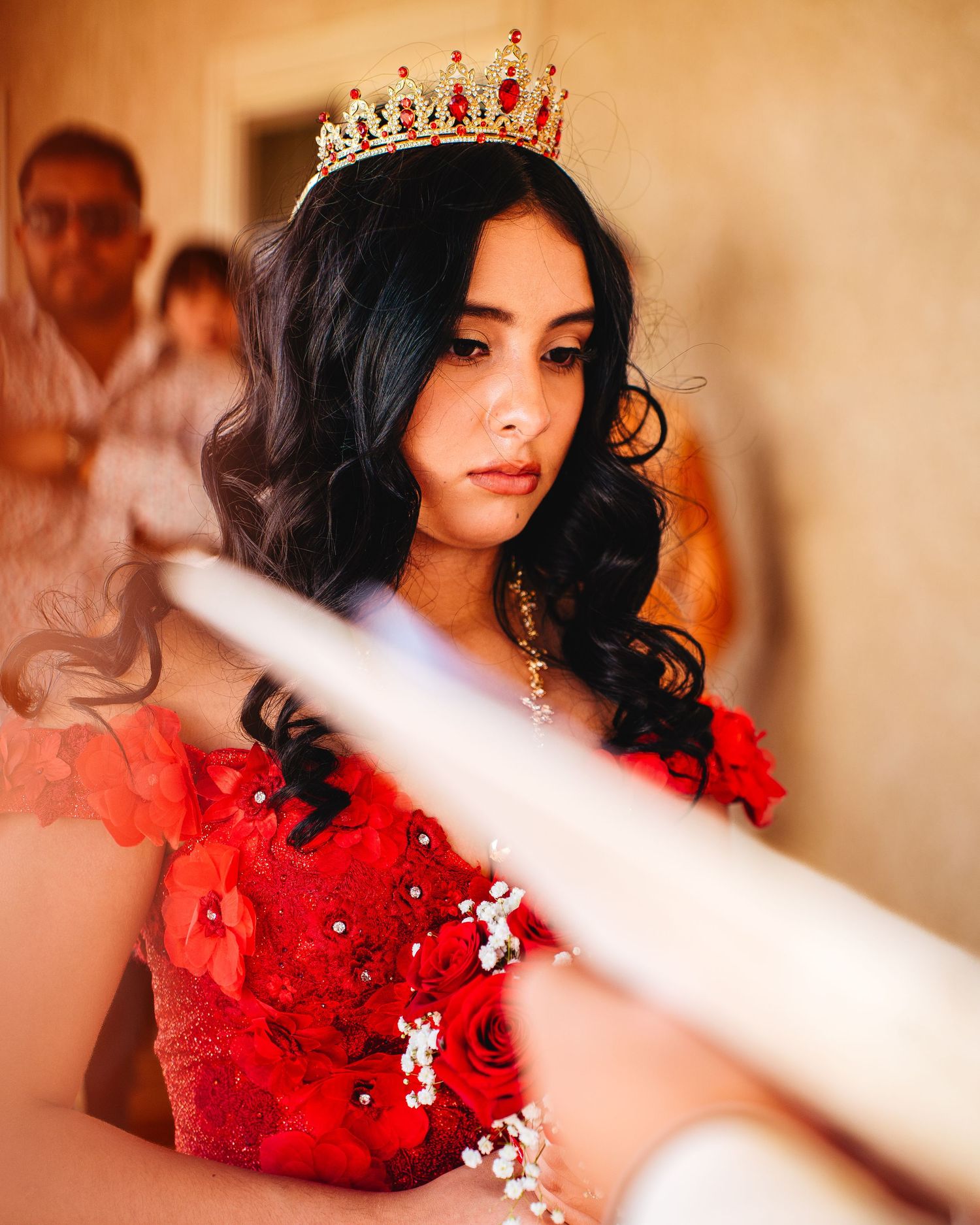 A glamorous figure in a sparkling red dress and crown poses elegantly in a soft-focus portrait with warm lighting.