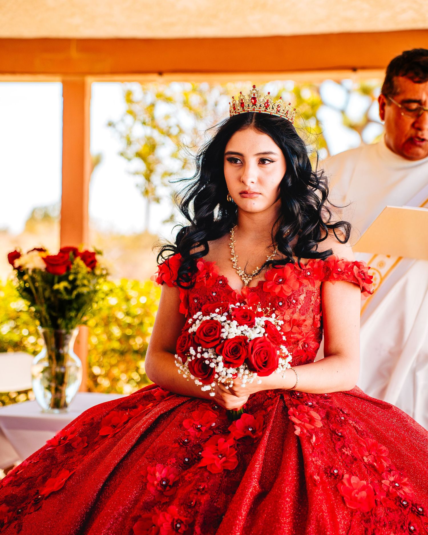 A stunning red ballgown with crystal embellishments and floral details is showcased in a quinceañera photoshoot.