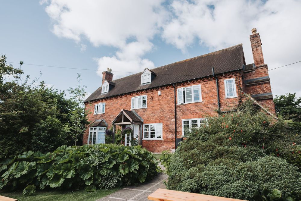 Traditional red brick English country house with white trim and lush green landscaping on a sunny day.