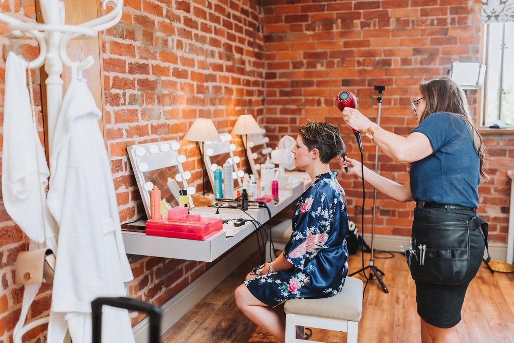 Wedding preparations in a rustic brick-walled room with white decor and natural lighting.