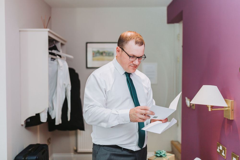 Person in white shirt and teal tie reading documents in a bedroom setting.