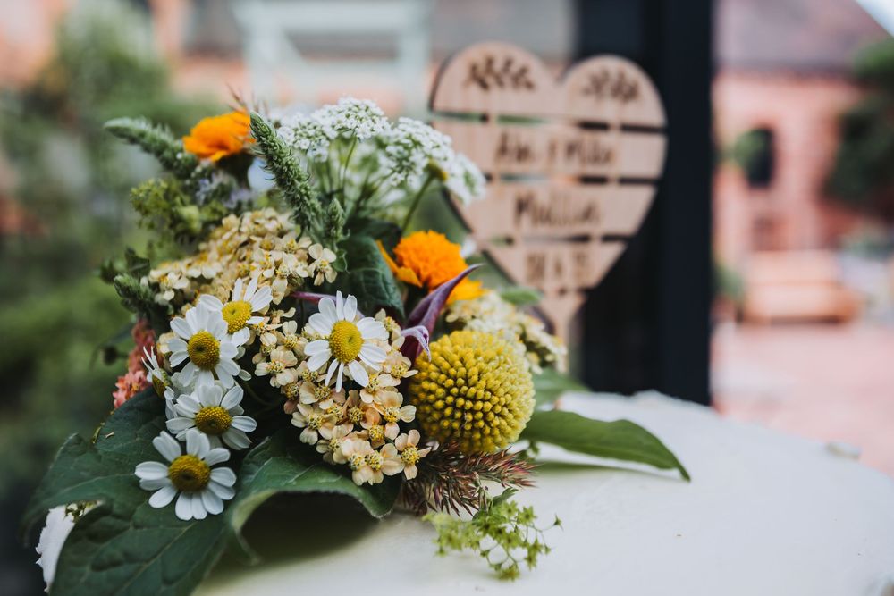 Delicate white and yellow floral arrangements with daisies and craspedia flowers displayed in a rustic setting.