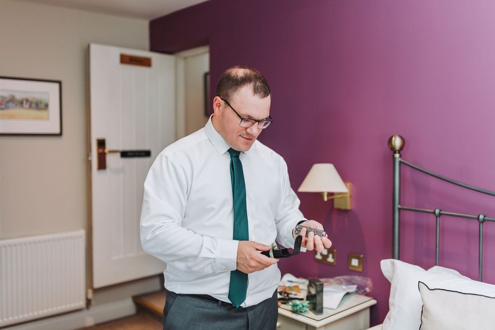 Person in formal attire checking items on a bed in a purple-walled room.