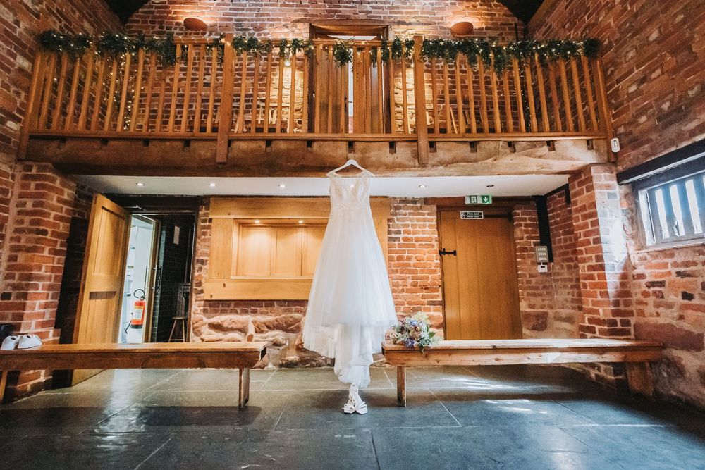 Rustic brick barn wedding venue interior with exposed beams, hanging white drapes, and warm ambient lighting.