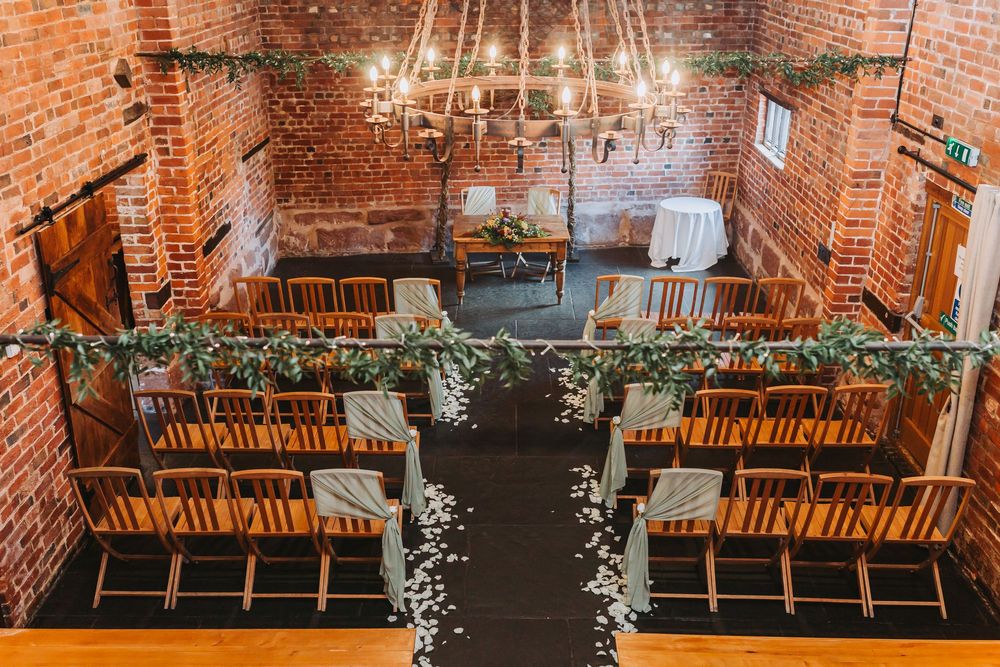 Rustic wedding venue with wooden chairs arranged in rows against exposed brick walls and hanging string lights.