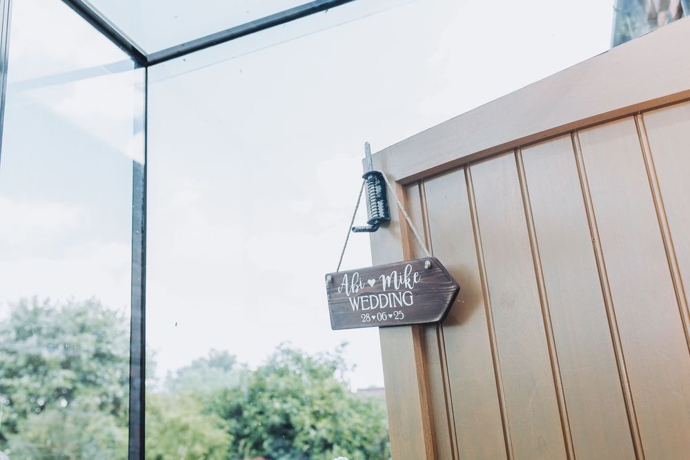 A modern glass-walled room with white furniture and decor overlooks a lush green landscape through large windows.
