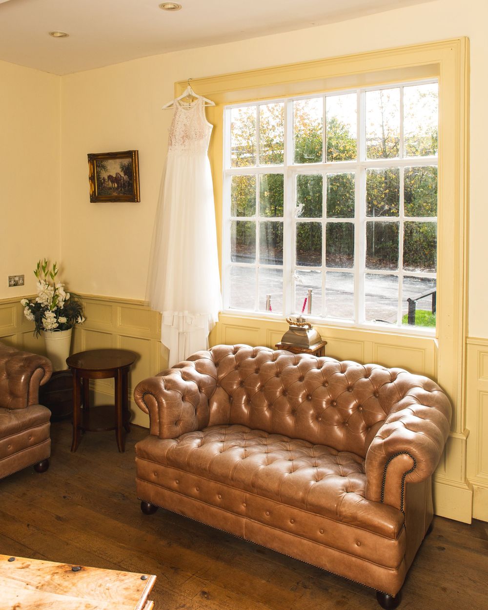 Elegant brown leather Chesterfield sofa in a bright living room with white walls and large windows.