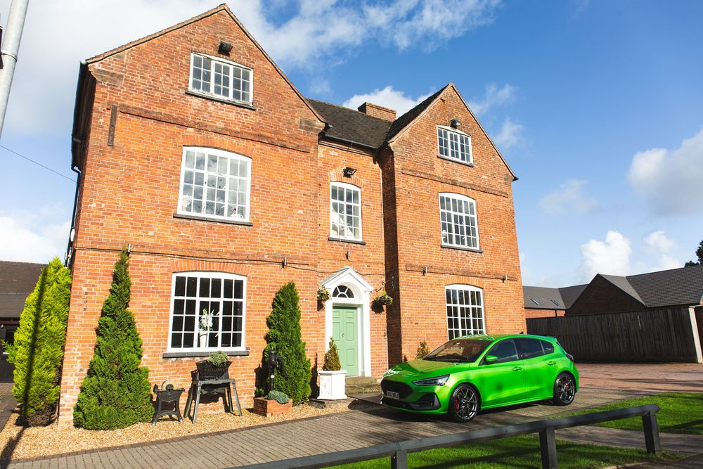 Beautiful red brick house with green door and bright green car parked in driveway on sunny day.