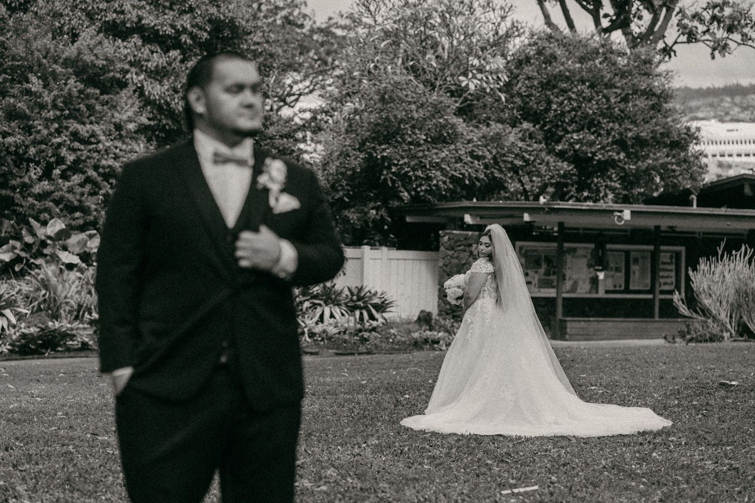 Black and white vintage photograph of a wedding scene in a garden with a bride in white gown and suited figure.
