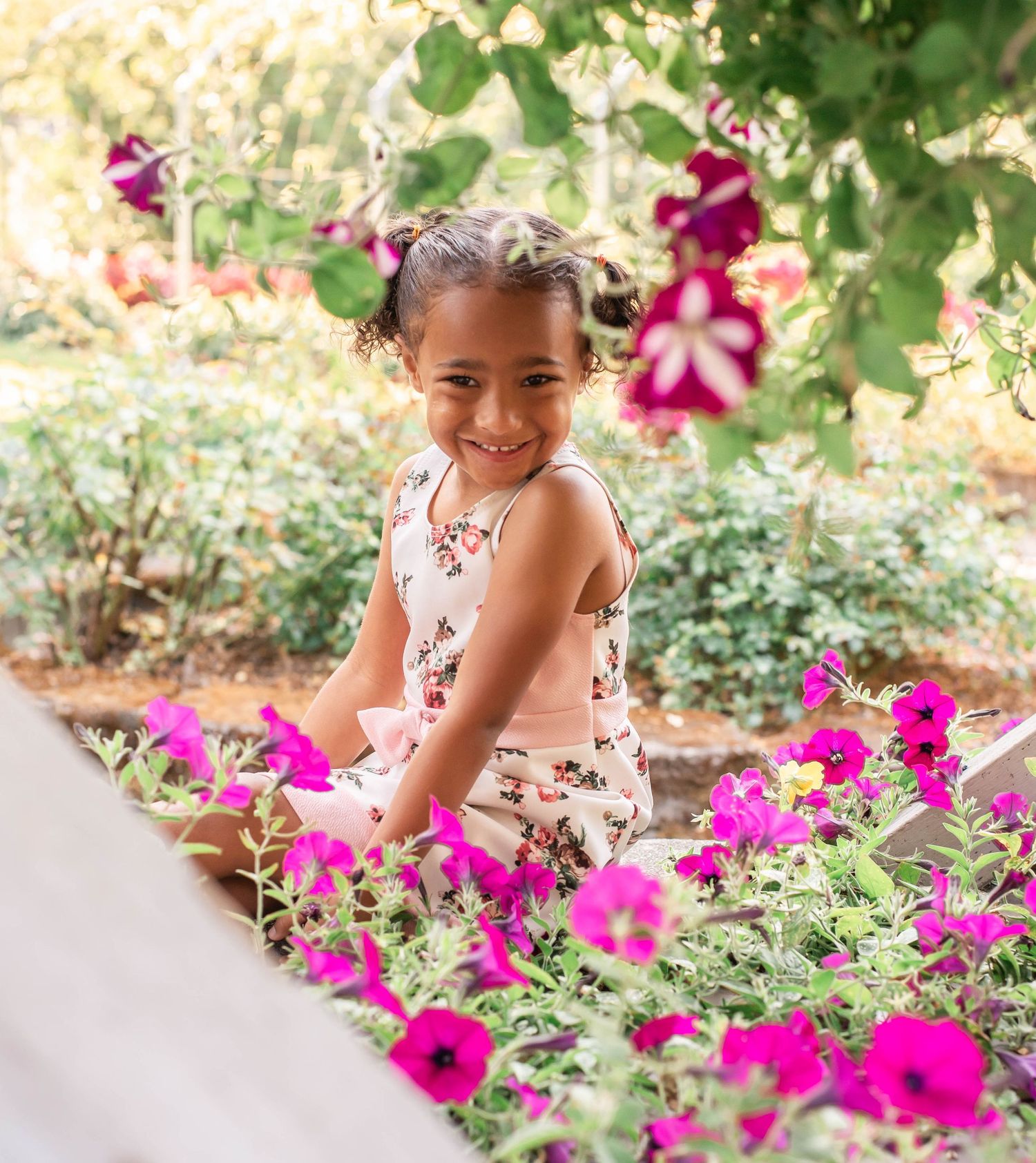 A joyful moment captured in a garden surrounded by vibrant pink petunias and lush greenery on a sunny day.