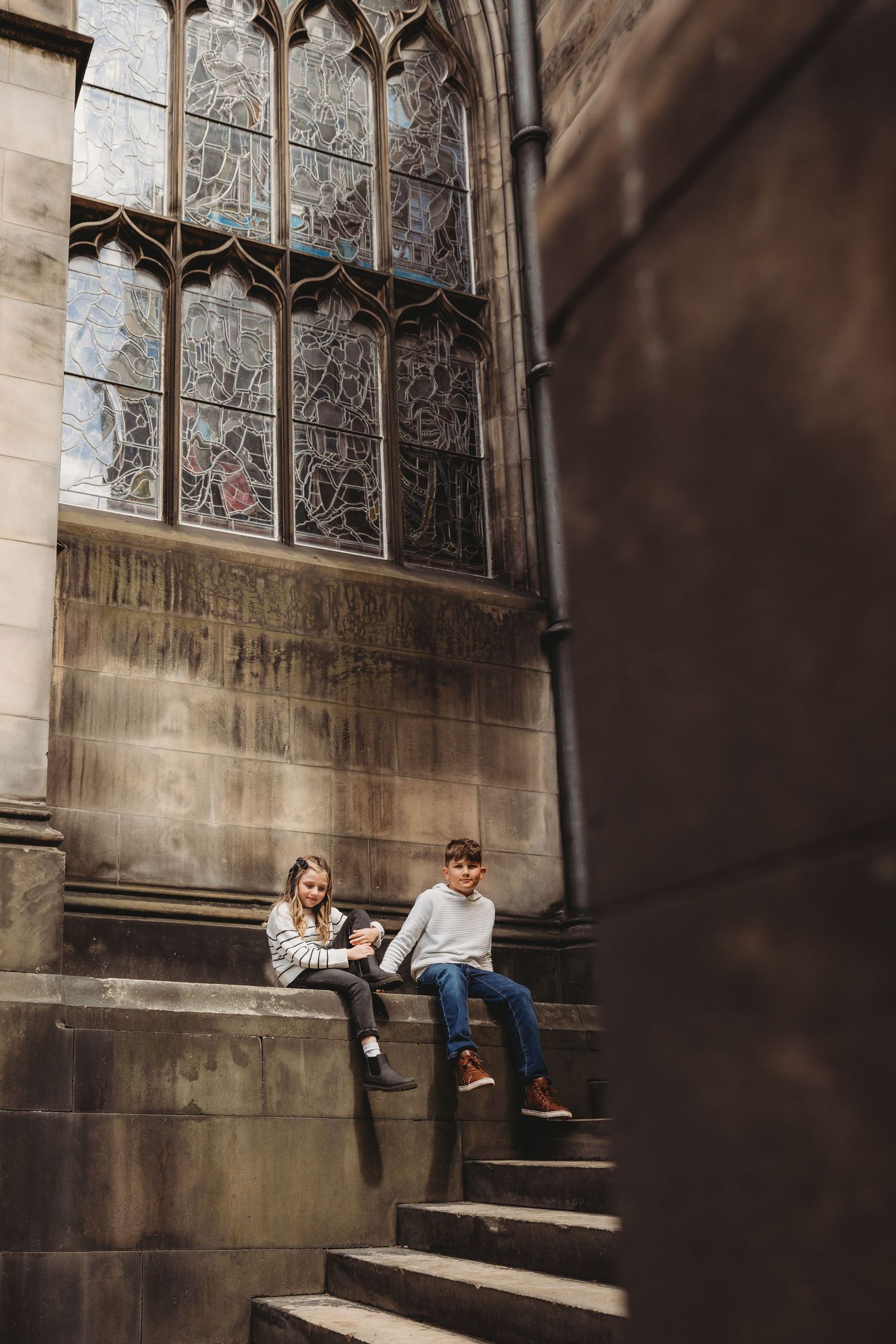People relaxing on stone steps against a gothic church wall with ornate stained glass windows in the background.