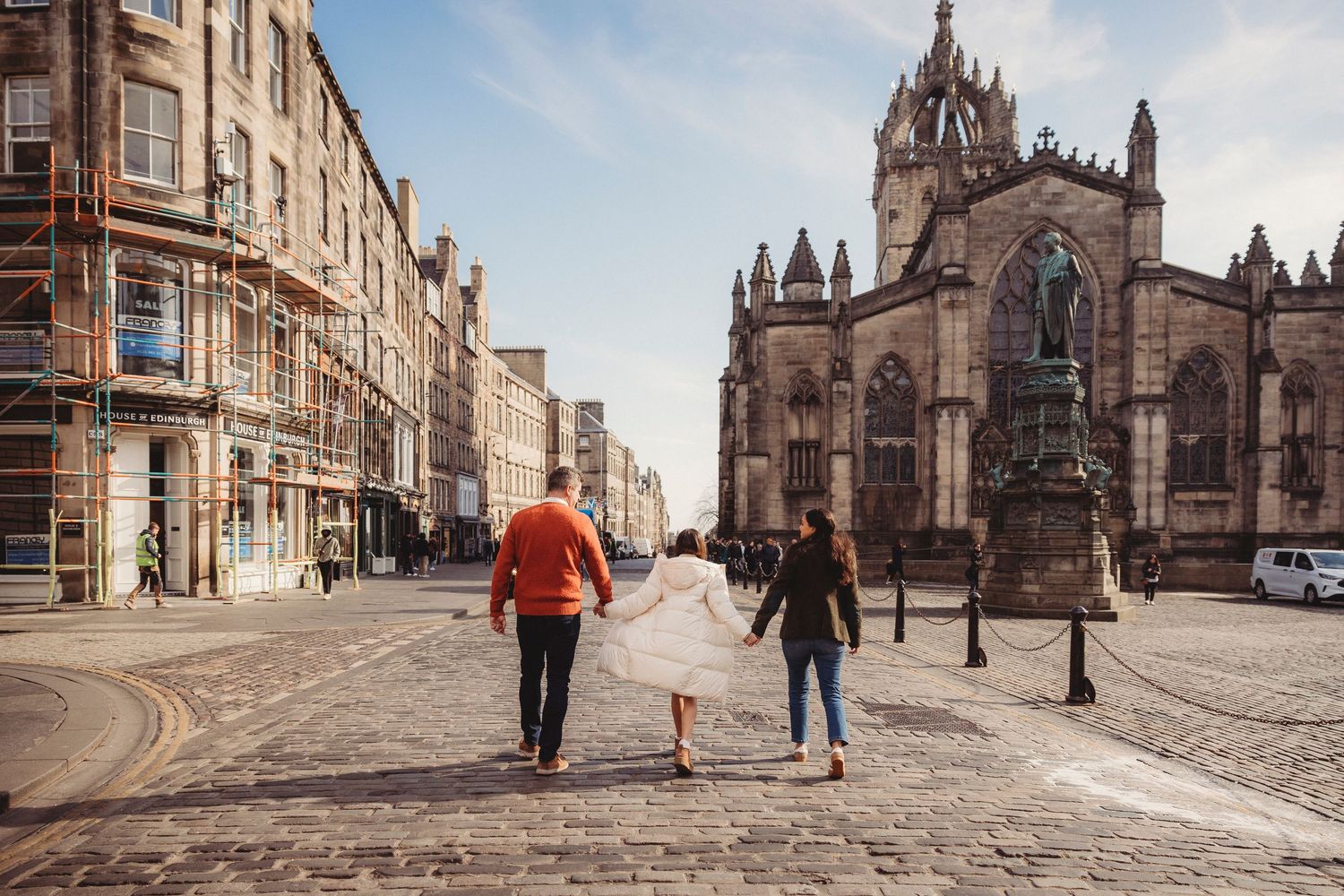 Historic stone buildings line a cobblestone street in Edinburgh's Old Town with St Giles Cathedral in the background.