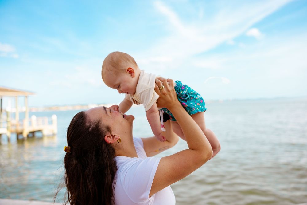 A parent lifts a small child playfully in the air at the beach during sunset.