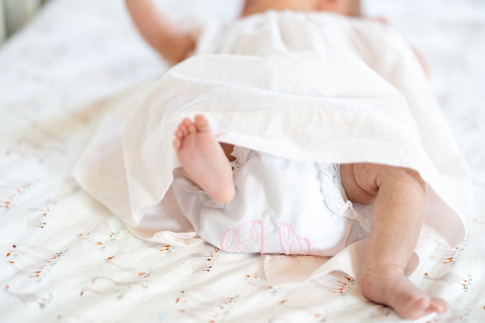 A newborn baby's tiny feet wrapped in soft white blankets with delicate details visible in natural light.