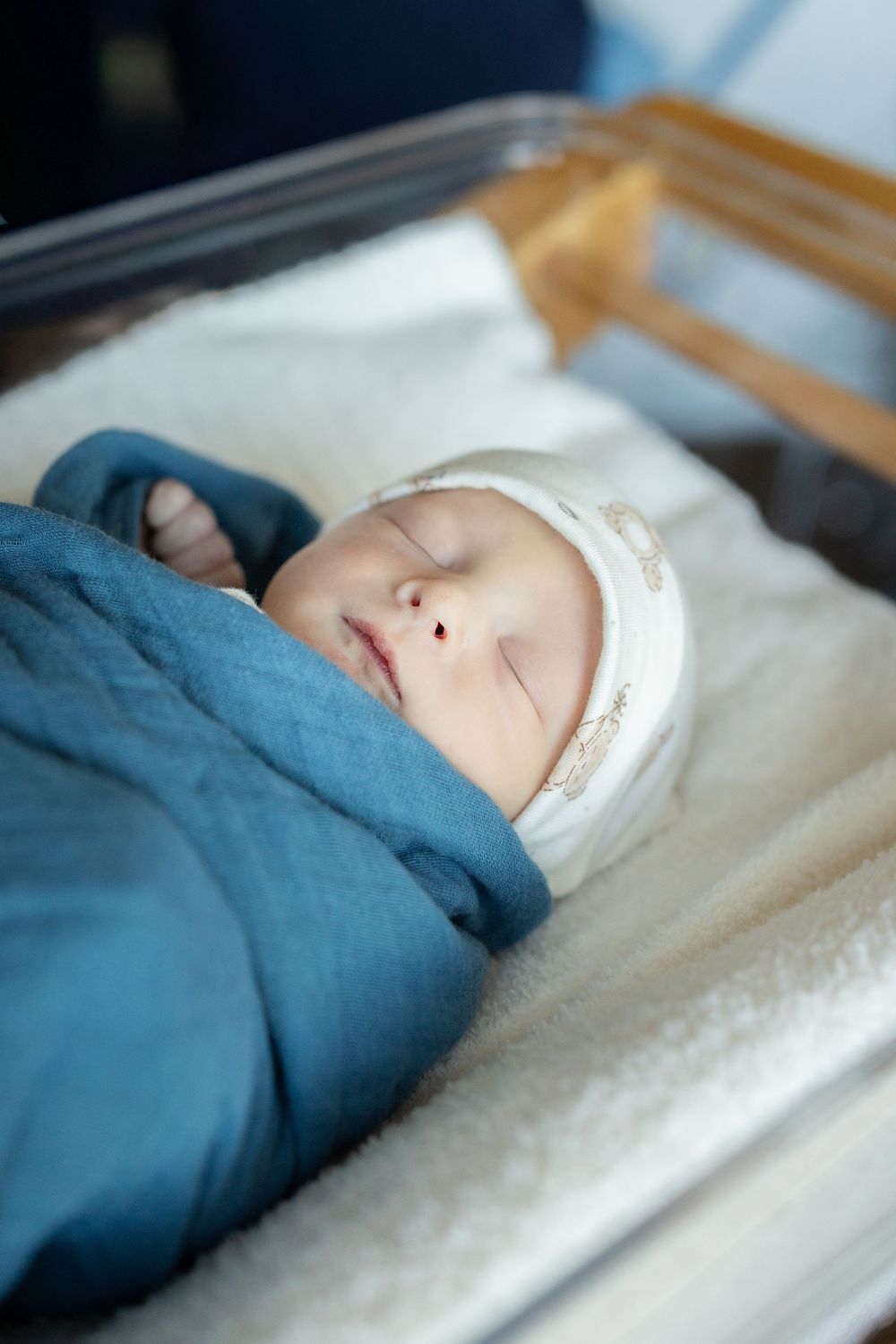 A sleeping baby wrapped in a soft blue blanket rests peacefully on white bedding.