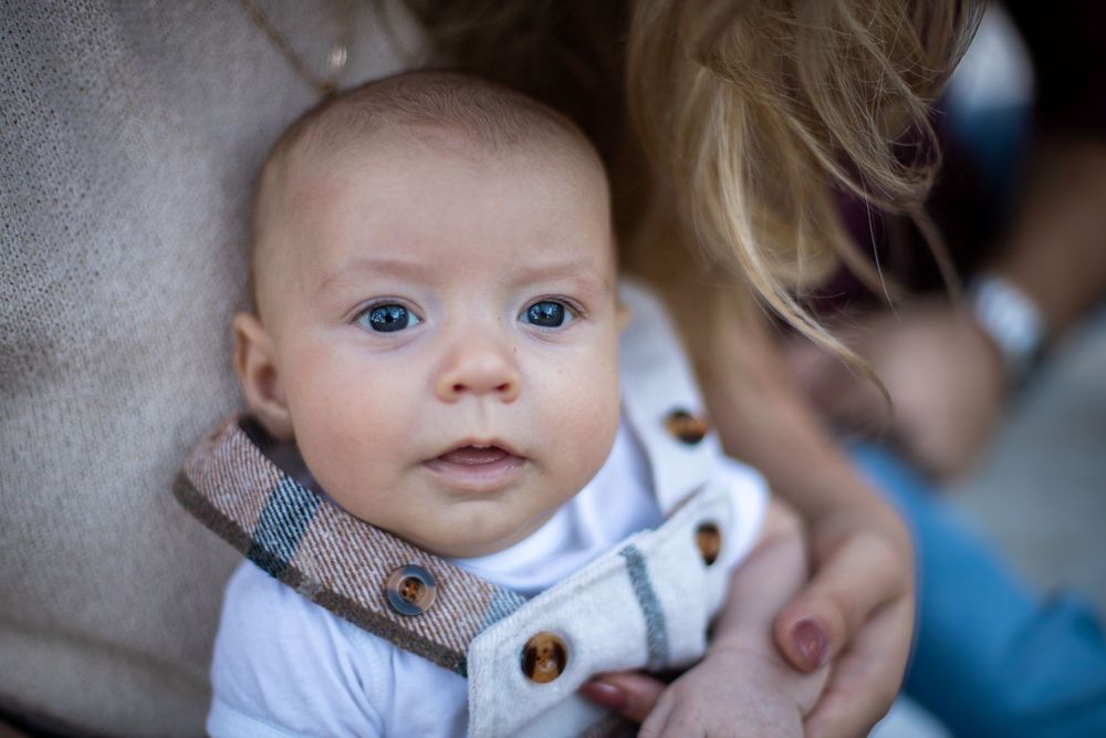 Baby wearing white outfit with brown buttons lying on beige fabric with soft focus background.