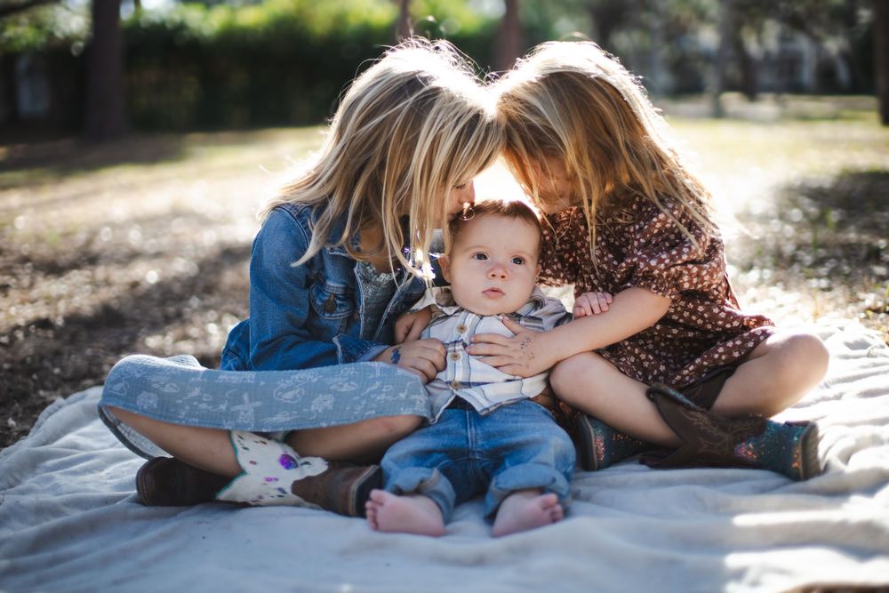 Family members lie together on a blanket outdoors during a sunny day photo session.