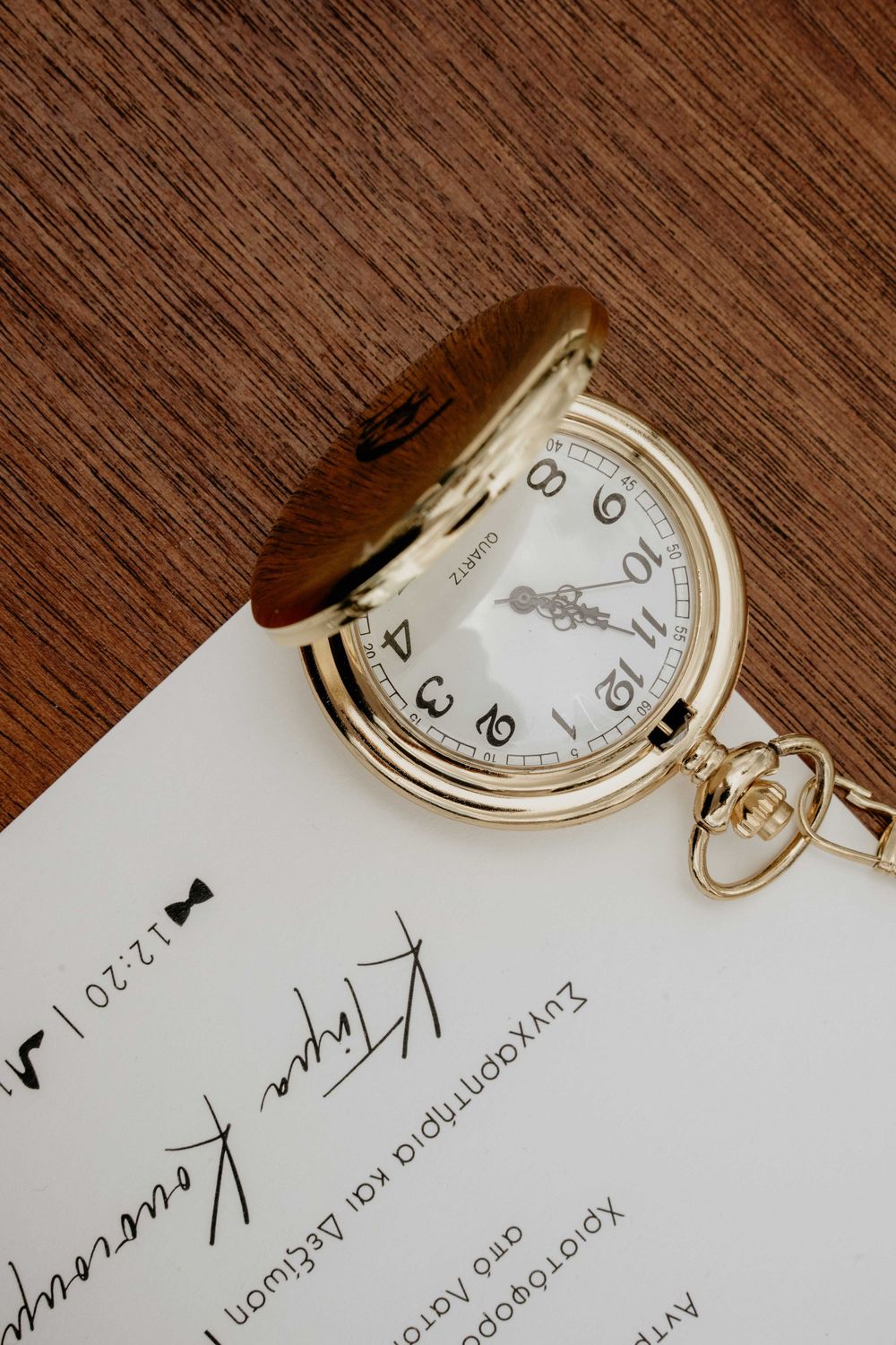 A vintage gold pocket watch rests on a white paper document against a dark wooden surface.