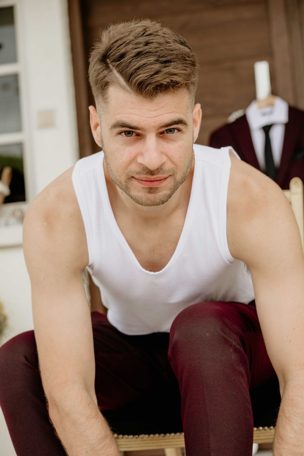 A person wearing a white tank top and burgundy pants sits casually on a wooden bench.