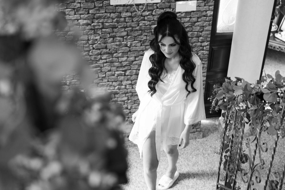 A woman in a white dress poses outdoors against a stone wall with decorative iron railings.