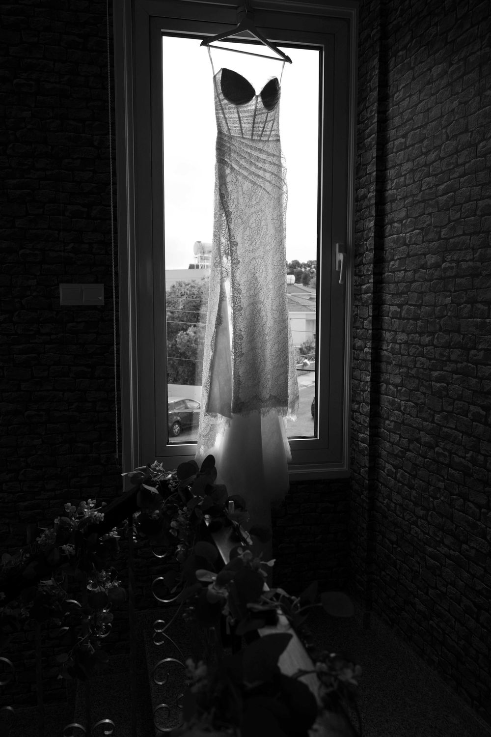 A white dress hangs by a window in a dark room with exposed brick walls, creating a moody silhouette.