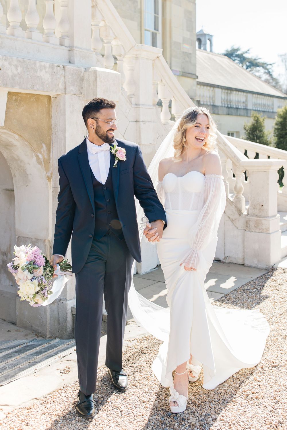 Wedding couple walking and laughing together on a stone balcony of a historic building.