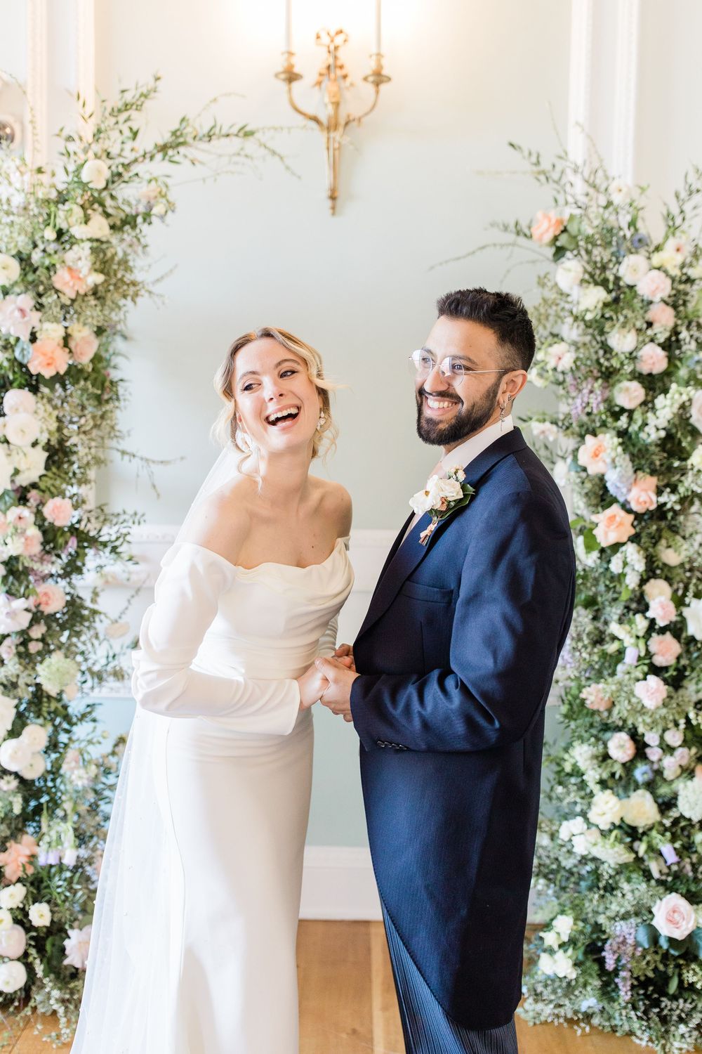 Joyful wedding couple dancing and laughing together surrounded by floral arrangements and chandeliers.