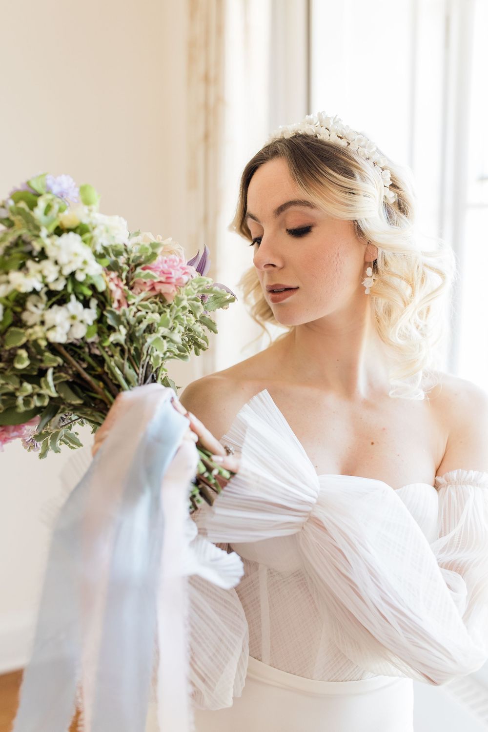 Elegant bridal portrait featuring a white off-shoulder gown, delicate tiara, and romantic floral bouquet in natural light.