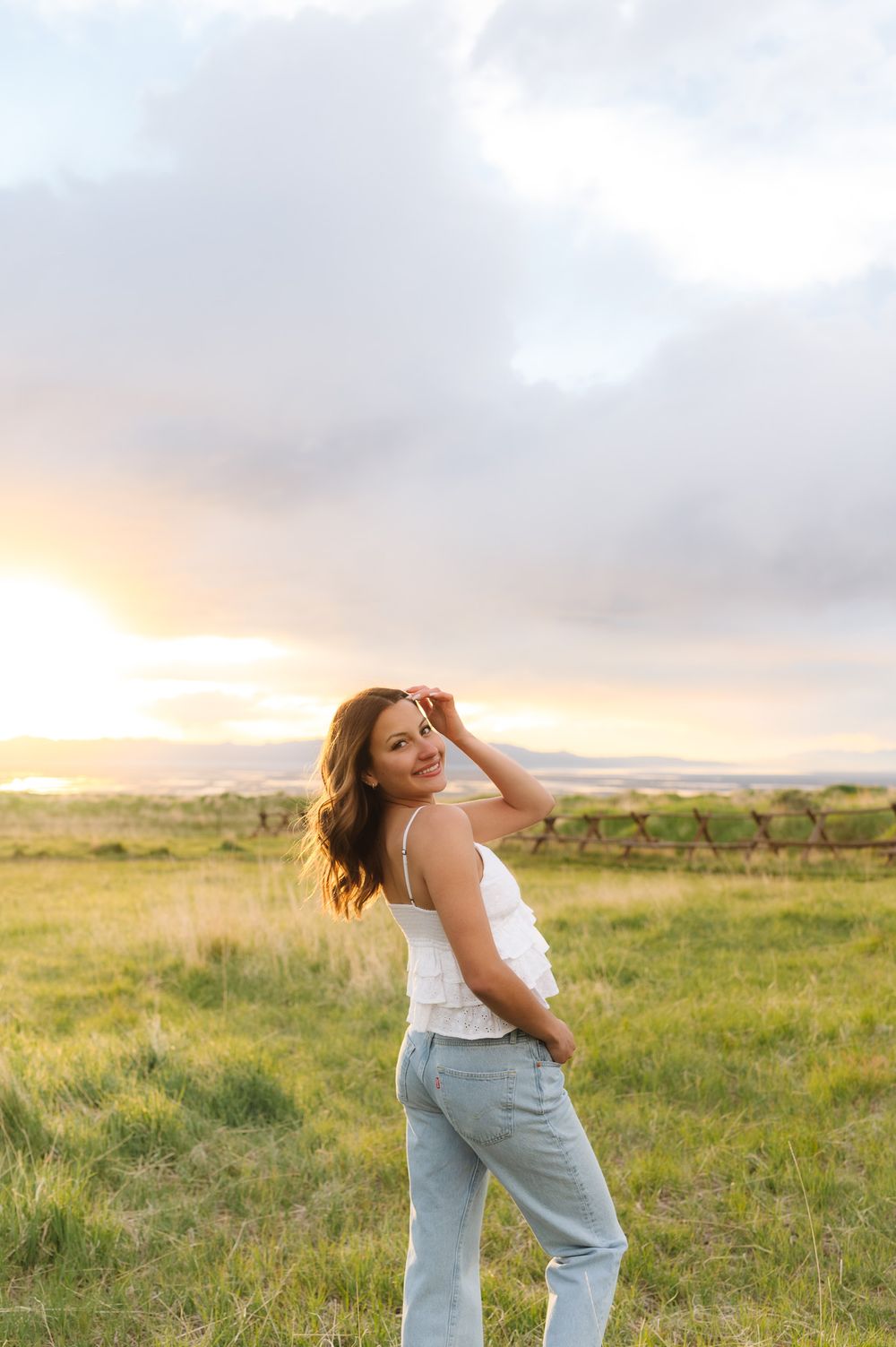 A person in a white top and jeans dances joyfully in a golden sunlit meadow at sunset.