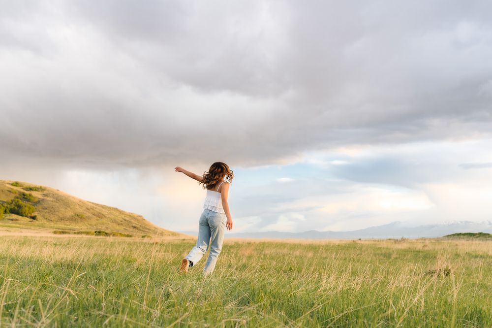 A person stands in a golden wheat field under dramatic cloudy skies with arms outstretched in North Salt Lake City