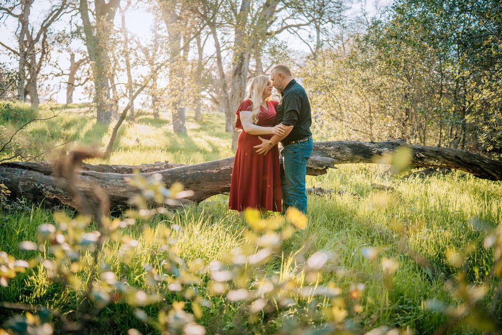 A couple shares a tender moment in a sunlit meadow filled with white wildflowers during springtime.