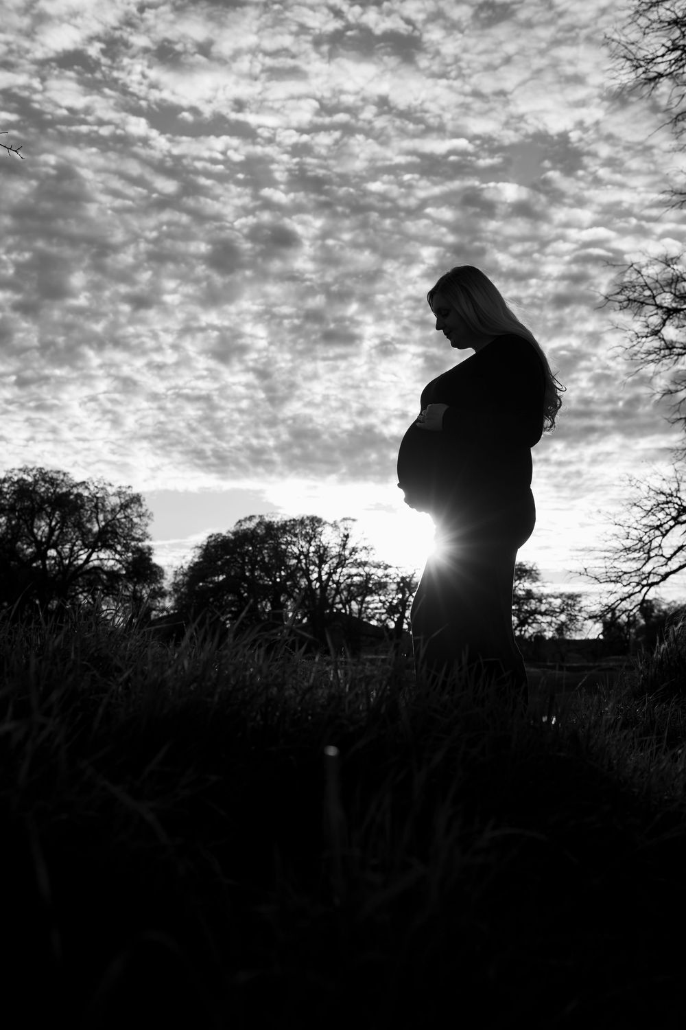 Dramatic silhouettes against a cloudy sunset sky showing a couple's maternity photoshoot.