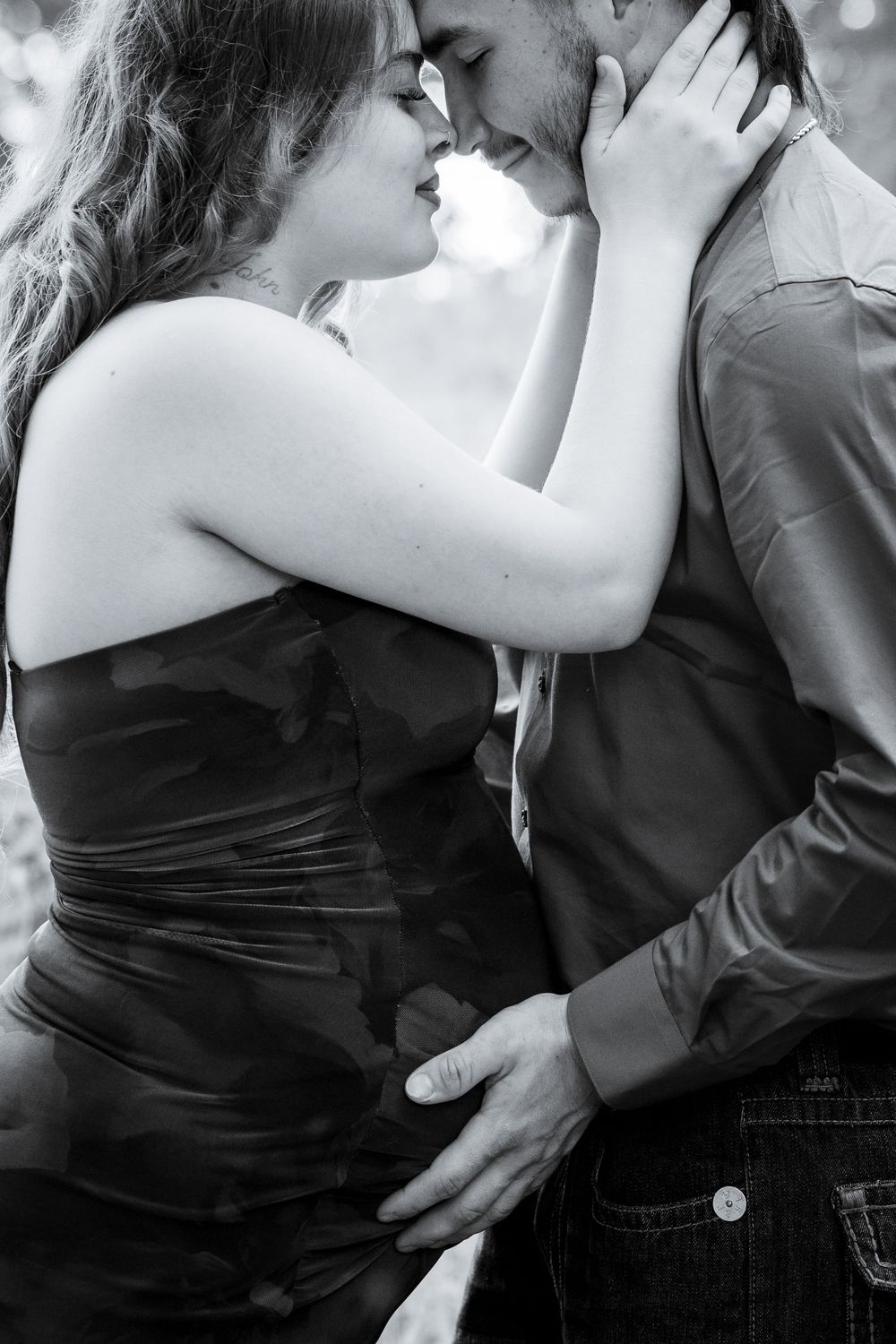 A romantic black and white image of a couple embracing tenderly in an outdoor setting.