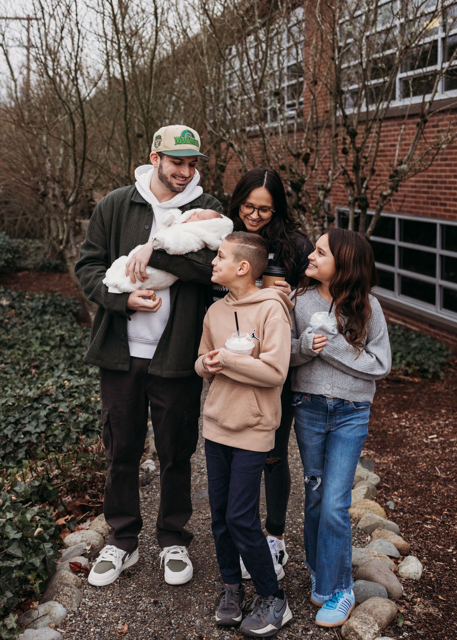 A group stands together outdoors near a brick building on a winter day, sharing warm embraces and conversation.