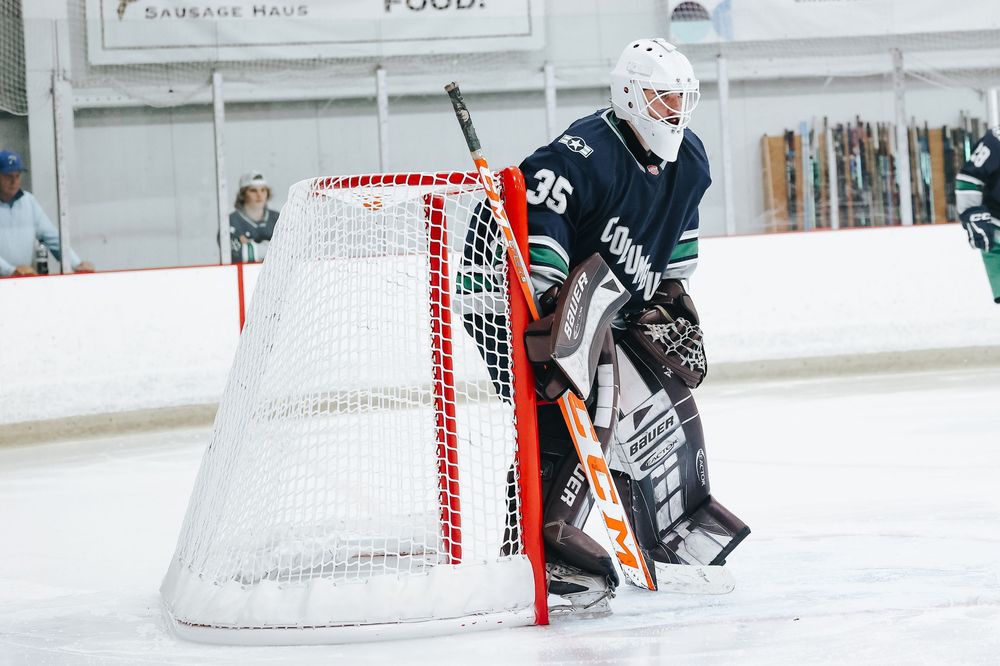 Hockey goalie crouching in defensive position near goal post during game.