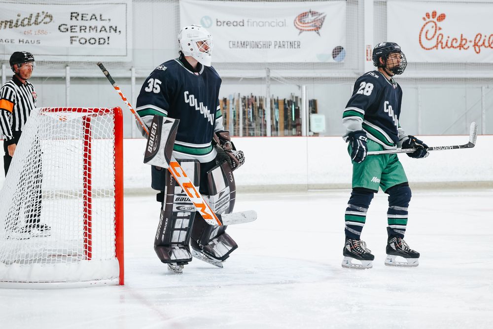 Hockey players in dark and light jerseys positioned around goal net during game.