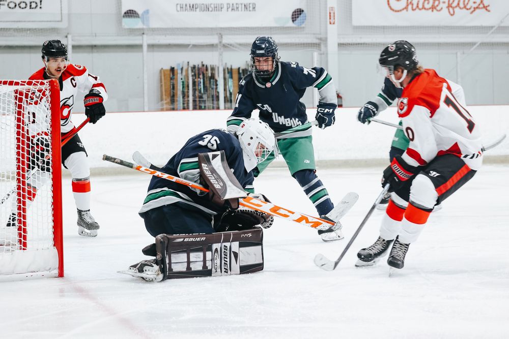 Hockey players in action with goalie defending against offensive play on ice.