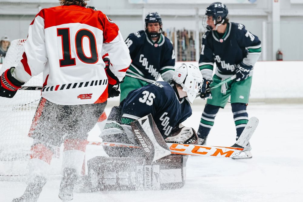 Ice hockey action shot with players spraying ice near the goal net.