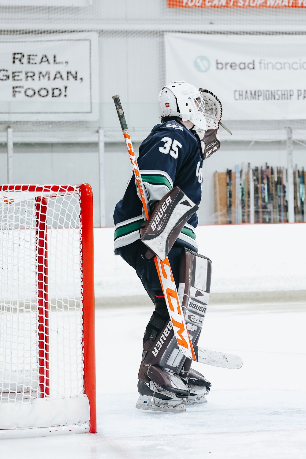 Hockey goalie in dark jersey positioned near goal post during game.