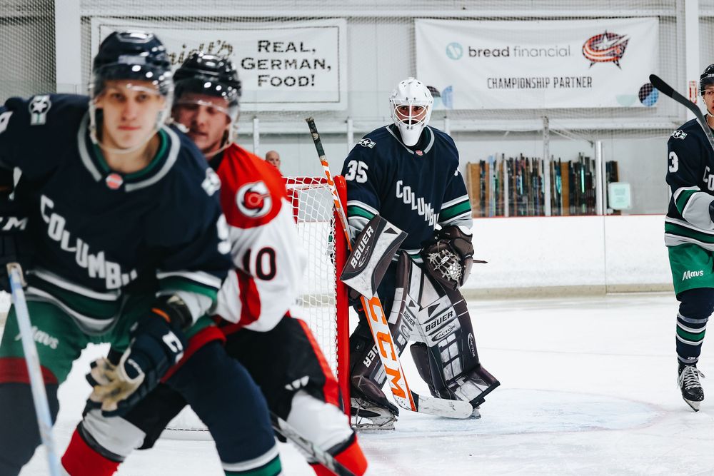 Hockey players in dark uniforms skate across ice during practice session.