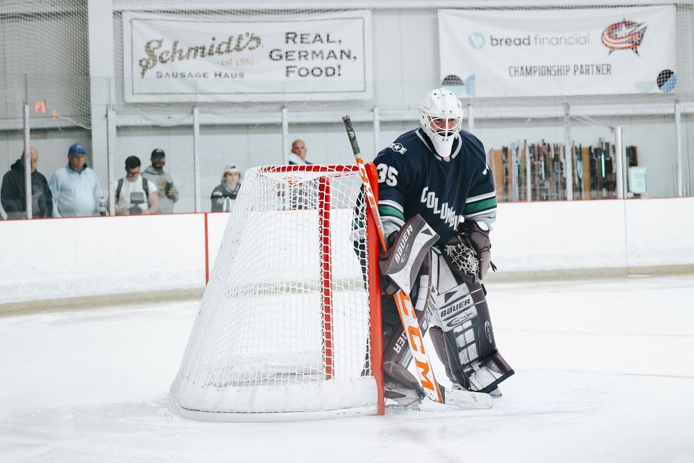 Hockey players in navy and white uniforms practice on an ice rink with red goal posts visible.