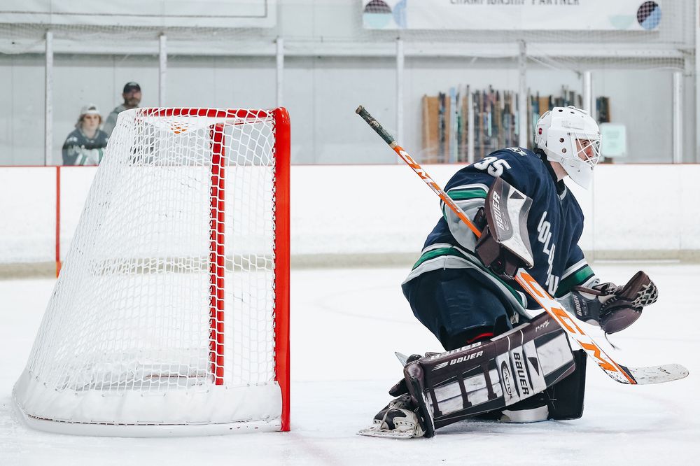 Hockey goalie makes diving save on ice during practice drill.
