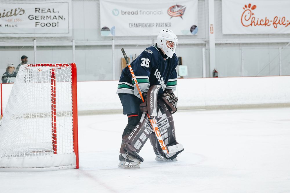 Hockey players practicing drills on indoor rink with advertisements visible on walls.