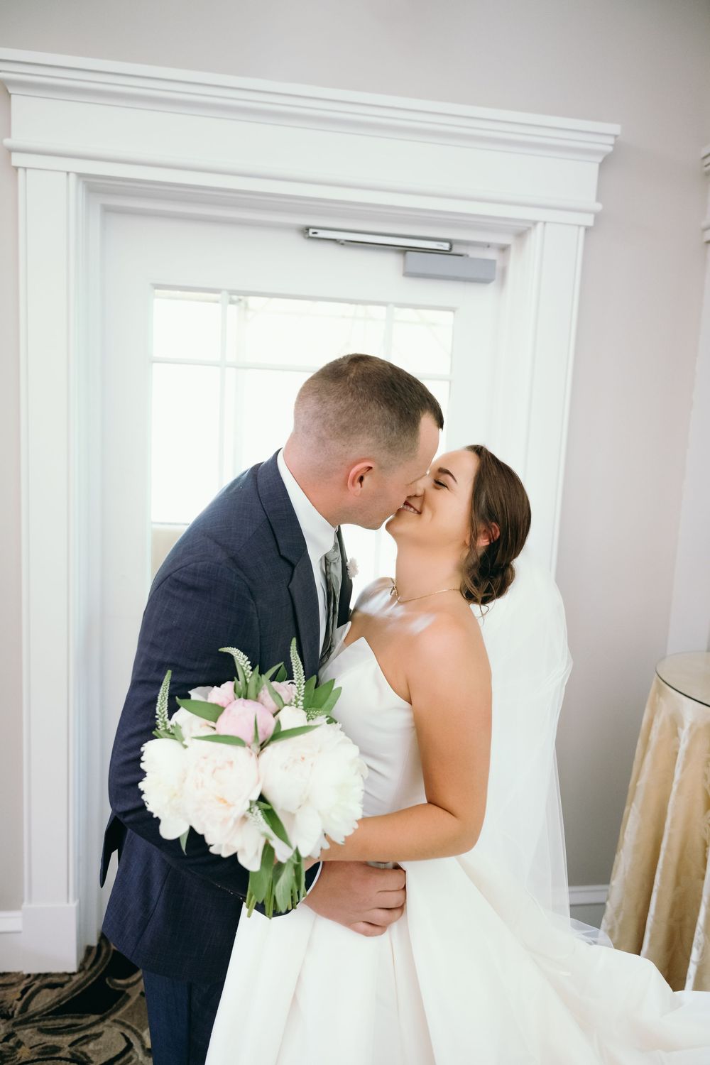 Romantic wedding moment captured in an elegant white room with natural window light.