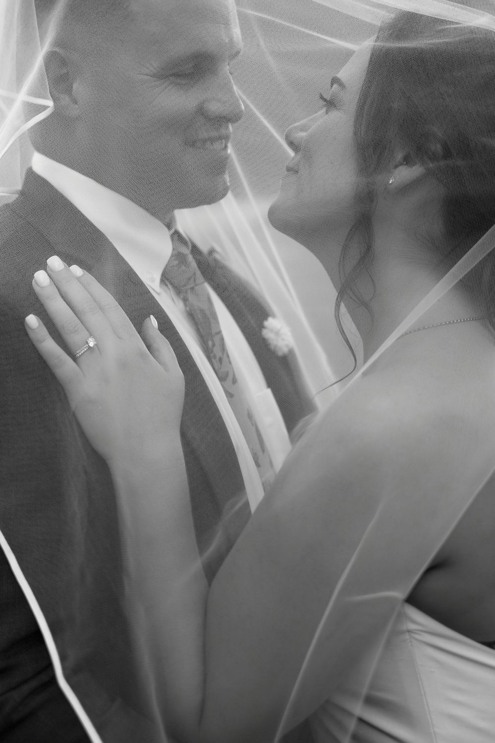 Romantic black and white portrait of newlyweds sharing intimate moment under wedding veil.