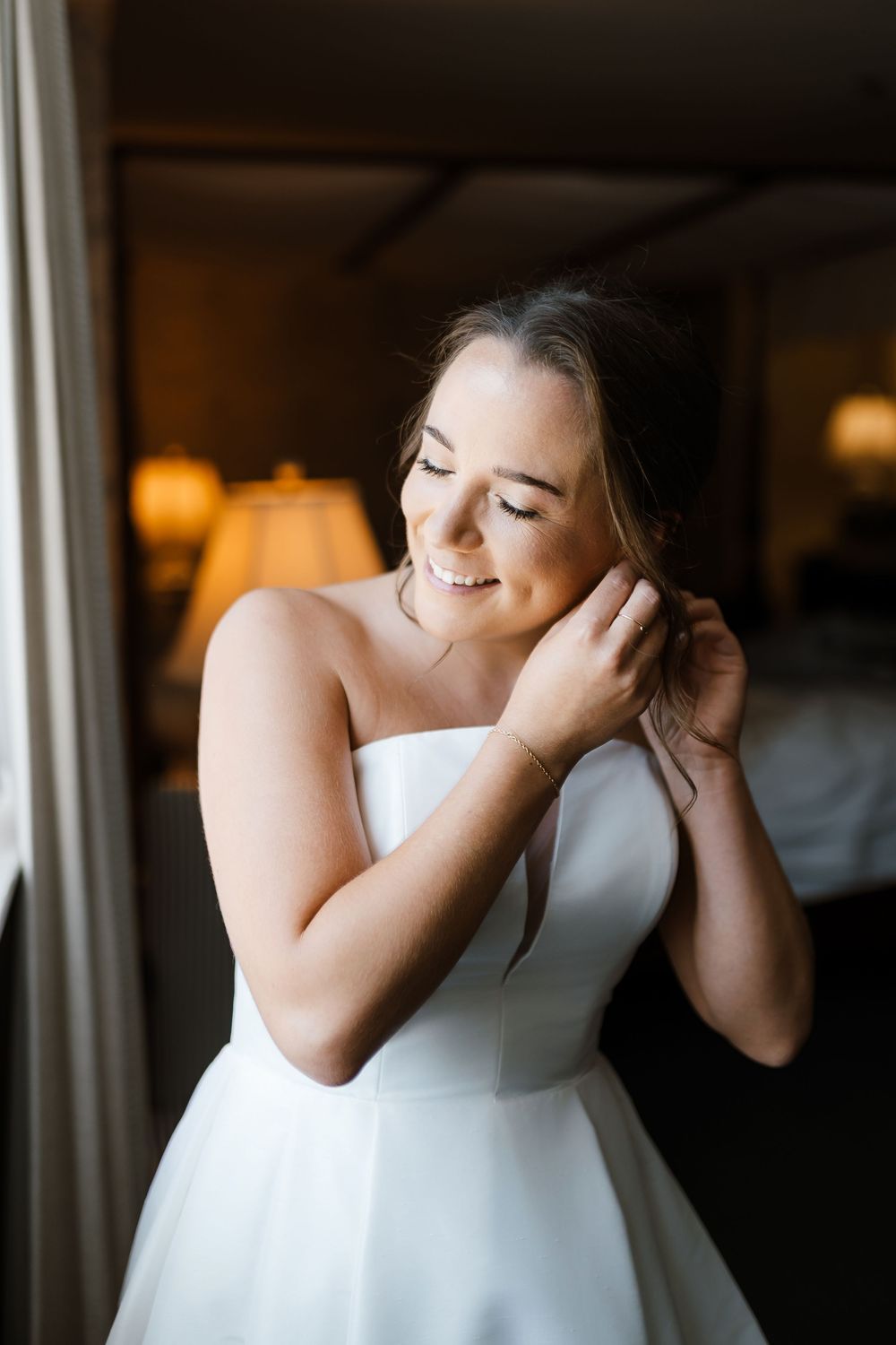 Bride in classic white strapless gown adjusts her earring while getting ready.
