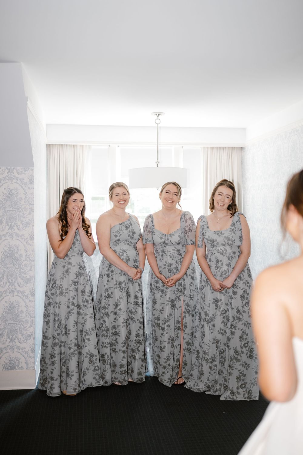Bridesmaids wearing matching gray floral dresses stand in a line at a wedding venue.