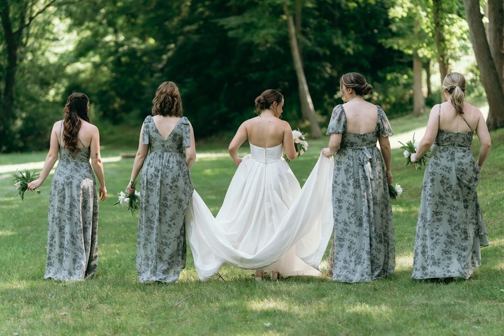 Bride and bridesmaids in floral dresses walking together on grass during outdoor wedding.