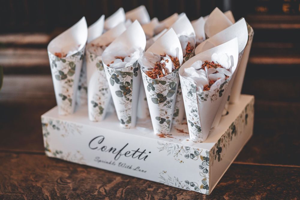 Rustic wooden box filled with floral patterned confetti cones for wedding celebration.